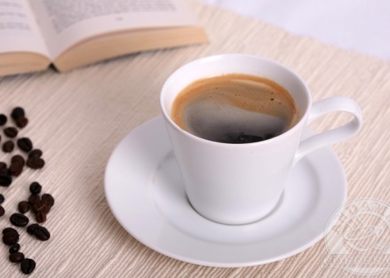 An Americano coffee on a table with a book and some coffee beans